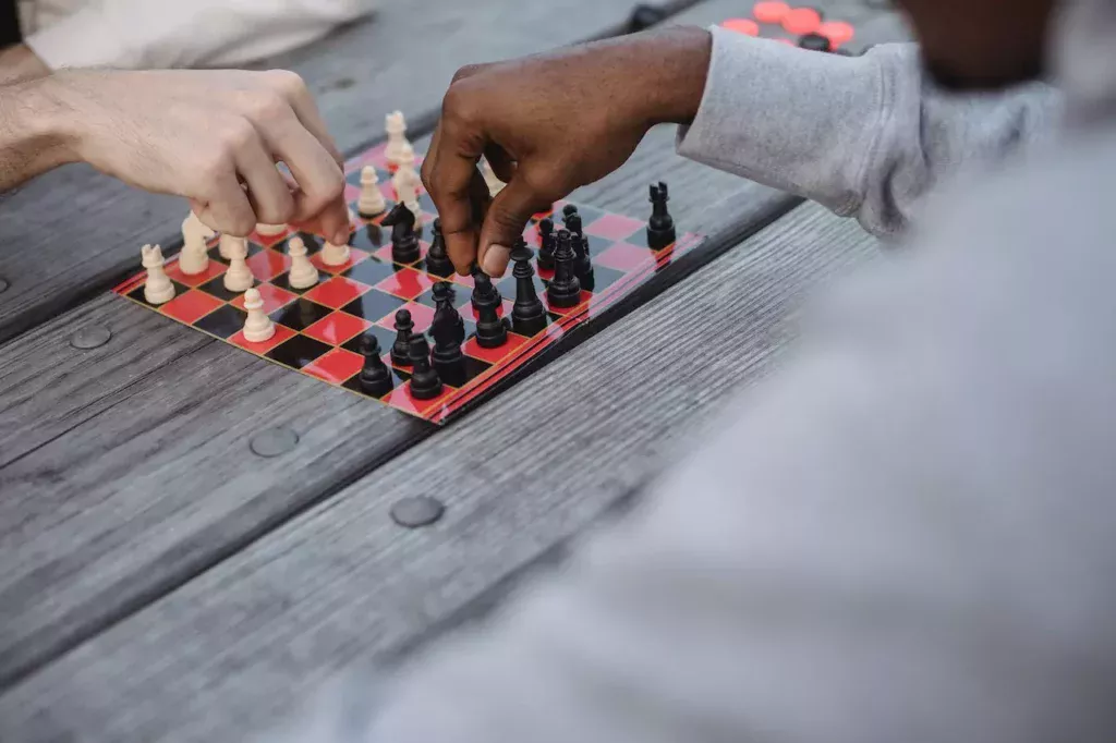 Strategic minds at play: Multiracial men engaged in a chess match at a wooden table, epitomizing the intellectual challenge and camaraderie of mindsports.