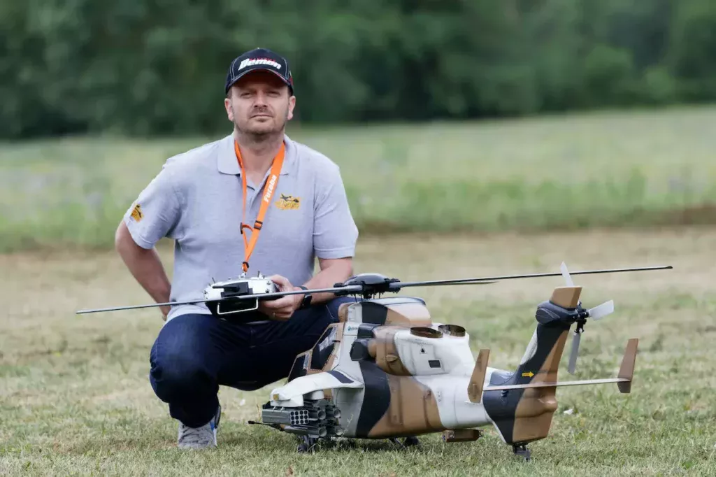 A man strikes a pose near a remote control helicopter toy, capturing the thrill and enthusiasm of remote control racing sports